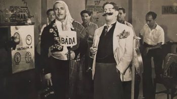 Fotografia em preto e branco de Castro Barbosa e Lauro Borges, radialistas, caracterizados em figurinos cômicos e diante de microfones, em um estúdio de rádio. Ao fundo, músicos e equipamentos de transmissão.